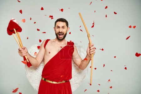Photo for Bearded man in cupid costume with heart-shaped arrows and bow screaming from excitement on grey - Royalty Free Image