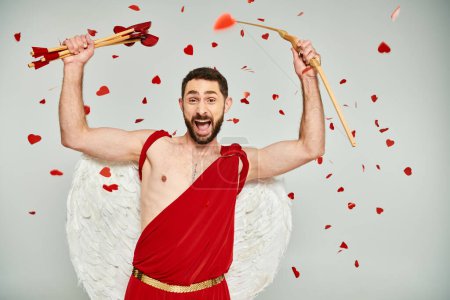 bearded man dressed as cupid with heart-shaped arrows and bow shouting from excitement on grey