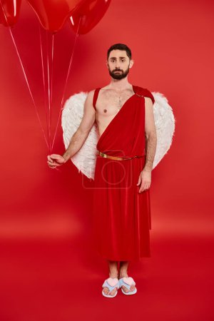 offended bearded man dressed as cupid with heart-shaped balloons on red, st valentines costume party