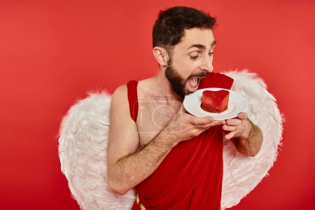 bearded cupid man with open mouth looking at delicious heart-shaped cale on red, st valentines treat
