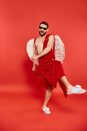 full length of overjoyed bearded cupid man dancing on red, st valentines day costume party