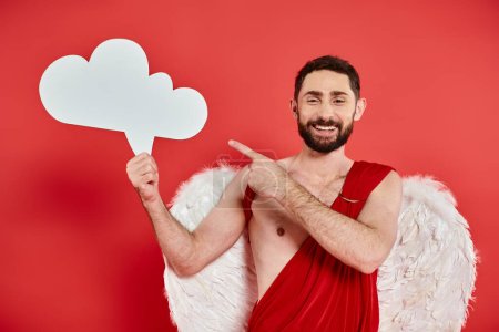 cheerful bearded man in cupid costume with white empty thought bubble showing idea sign on red