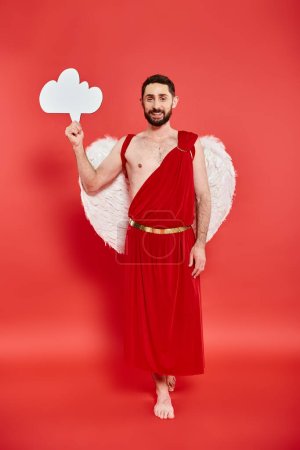 full length of barefoot bearded man dressed as cupid with white empty thought bubble on red