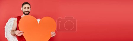 romantischer bärtiger Mann im Amor-Kostüm mit riesigem Papierherz auf rotem Grund, Valentinstag, Banner