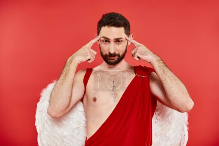 thoughtful bearded man in cupid costume touching head looking at camera on red, st valentines day
