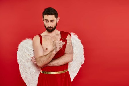 strict serious bearded man in cupid costume showing attention gesture on red, st valentines concept