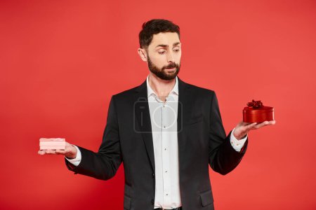elegant bearded businessman in black suit choosing Saint Valentines day present on red backdrop