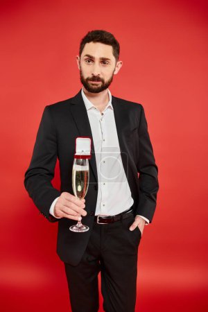 man in black suit with champagne glass and gift box with jewelry ring on red, st valentines day