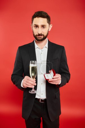 smiling bearded man in elegant attire with champagne and jewelry box on red, Saint Valentines day