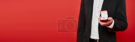 cropped view of wealthy elegant man with ring in jewelry box on red, horizontal banner
