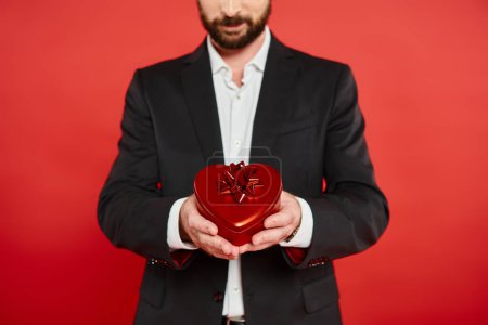 Photo for Cropped view of bearded elegant man holding st valentines day present in heart-shaped gift box - Royalty Free Image