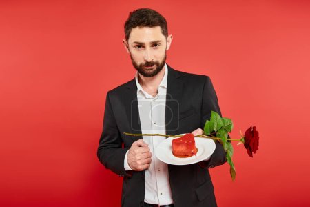 handsome bearded man holding plate with rose and heart-shaped cake on red, st valentines day