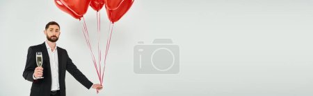 Photo for Stylish bearded man with red heart-shaped balloons and champagne glass on grey, horizontal banner - Royalty Free Image