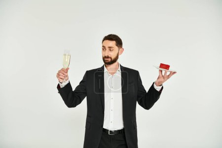 Photo for Stylish man in black suit with champagne glass and heart-shaped cake on grey, Saint Valentines day - Royalty Free Image