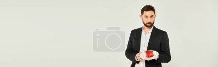 Photo for Charismatic elegant man with delicious heart-shaped st valentines cake on grey, horizontal banner - Royalty Free Image