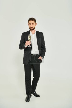 handsome businessman in black suit with champagne and hand in pocket on grey, st valentines concept