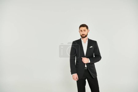 good-looking bearded businessman in black stylish suit standing and looking away on grey backdrop
