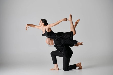Anmutiger Tanz, junges Paar, das im Studio vor grauem Hintergrund eine akrobatische Übung vollführt