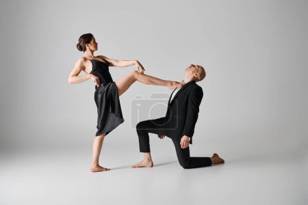 joven mujer descalza en vestido negro realizando baile apasionado con el hombre sobre fondo gris