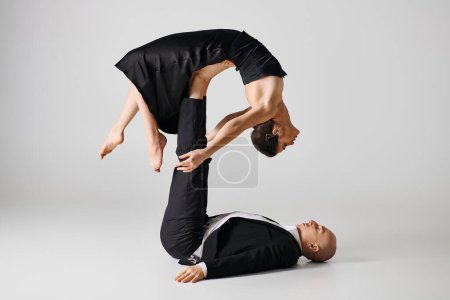 flexible young woman in black attire balancing on bare feet of her dancing partner on grey backdrop