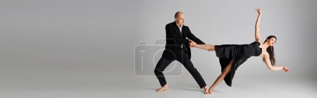 Photo for Flexible young woman in black dress balancing on her bare feet near dancing partner of grey, banner - Royalty Free Image