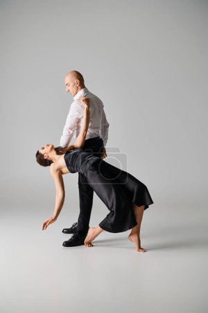 Foto de Morena bailarina femenina en vestido negro sosteniendo rosa roja y equilibrando en vueltas de hombre sobre fondo gris - Imagen libre de derechos