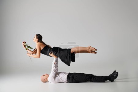 Foto de Bailarina masculina acostada en el suelo y levantando el cuerpo de la mujer en vestido con rosa durante el rendimiento - Imagen libre de derechos