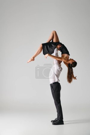 man in suit lifting body of woman in black dress during dance performance on grey backdrop