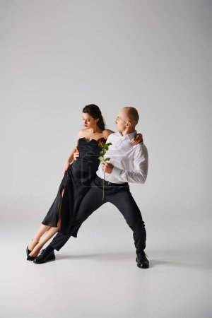 Elegant dance motion of young dancers, woman holding red rose and man in formal attire in studio