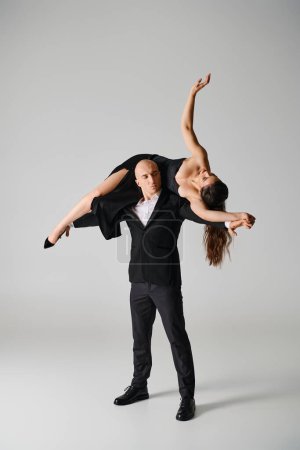 strong male dancer lifting brunette woman in dress and high heels in studio on grey background