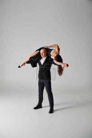 strong male dancer lifting brunette woman in dress and high heels on grey backdrop in studio