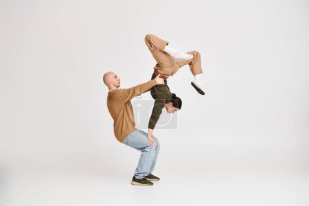 Couple in casual attire performing an intricate acrobatic balance in studio on grey background