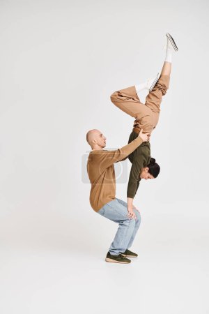 Couple in casual attire performing an intricate acrobatic balance in studio on grey background