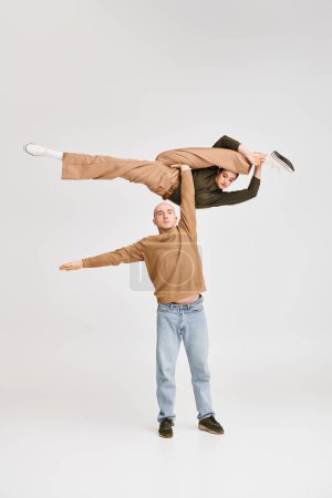 Couple in casual attire performing dynamic acrobatic balance in studio on grey background