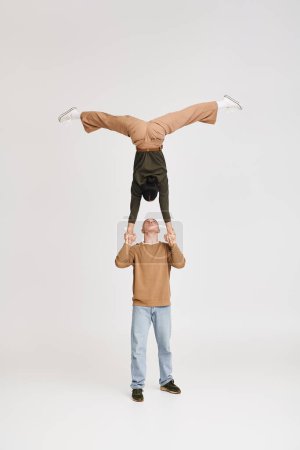 Artistisches Akrobat-Duo mit Frau im Kopfstand unterstützt von kniendem Mann im Studio vor grauem Hintergrund