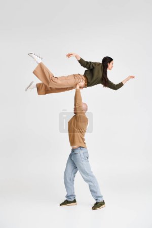 artistic acrobat duo with man lifting and supporting young woman in studio on grey backdrop