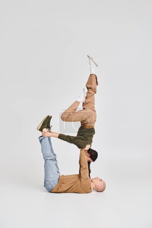 Akrobatisches Paar, junge brünette Frau in lässiger Kleidung balanciert mit Unterstützung ihres Partners im Studio