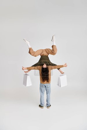 Frau hält Einkaufstüten und balanciert kopfüber mit Unterstützung ihres akrobatischen Partners im Studio
