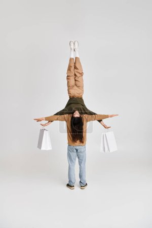 woman holding paper bags and balancing upside down with support of acrobatic partner in studio