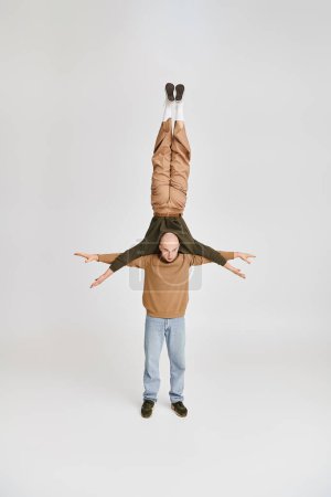 starker Mann in Freizeitkleidung unterstützt Körper des Akrobat-Partners beim Proben im grauen Studio