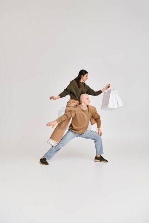 Foto de Rendimiento acrobático de pareja artística, mujer con bolsas de compras equilibrio en el cuerpo del hombre en gris - Imagen libre de derechos