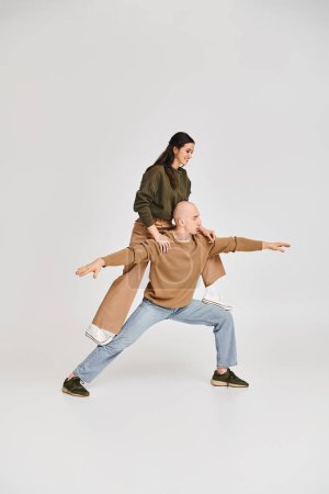 acrobatic performance of artistic couple, woman in casual clothes balancing on legs of man on grey