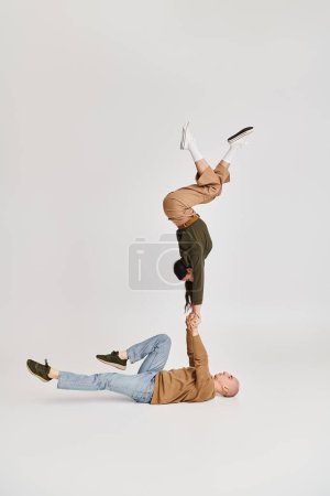 acrobatic performance of artistic couple, woman in casual clothes balancing on hands of man on grey