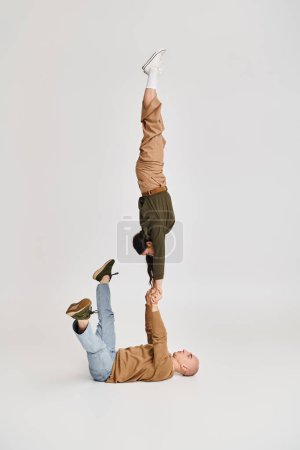 Akrobatische Darbietung eines künstlerischen Paares, Frau in Freizeitkleidung balanciert auf den Händen eines Mannes auf grau