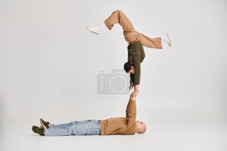 Foto de Actuación acrobática de pareja artística, mujer en ropa casual equilibrio en las manos del hombre en gris - Imagen libre de derechos