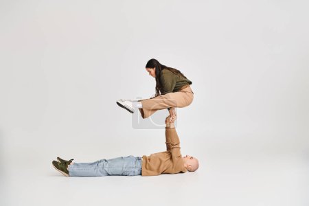 acrobatic performance of young couple, woman in casual clothes balancing on hands of man on grey
