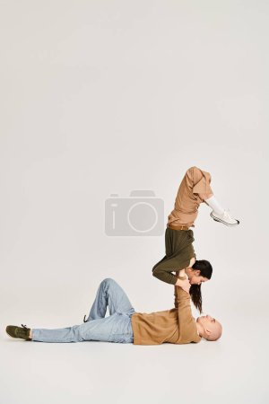 Foto de Morena mujer en casual desgaste equilibrio en las manos de hombre fuerte, pareja de acróbatas en el estudio - Imagen libre de derechos