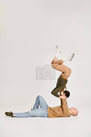 Foto de Morena joven en ropa casual equilibrio en las manos de un hombre fuerte, pareja de acróbatas en el estudio - Imagen libre de derechos