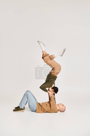 young female acrobat in casual wear balancing on hands of strong man, couple rehearsing in studio