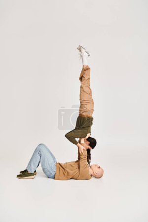 brünette Akrobatin in Freizeitkleidung balanciert auf den Händen eines starken Mannes, Paar probt im Studio